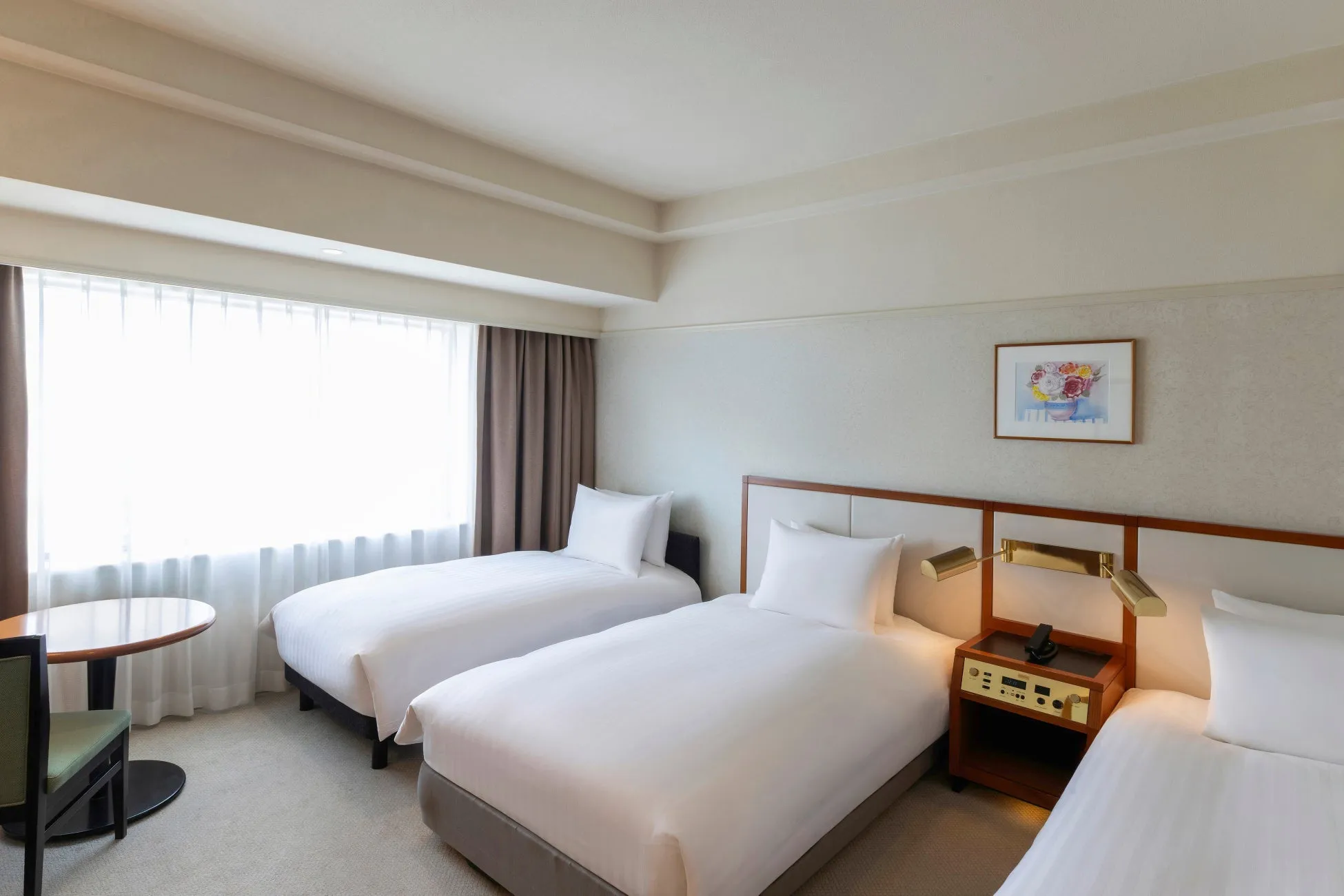 3つのベッドが配置されたホテルの客室。窓から明るい光が差し込み、シンプルで清潔感のある内装が特徴的です。