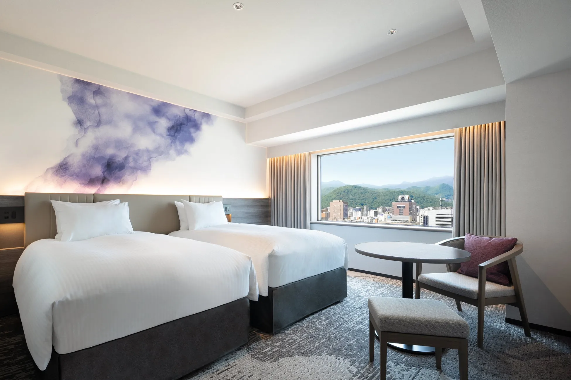 ホテルの一室の写真。ツインベッドが2つあり、窓からは街並みと山が見える。