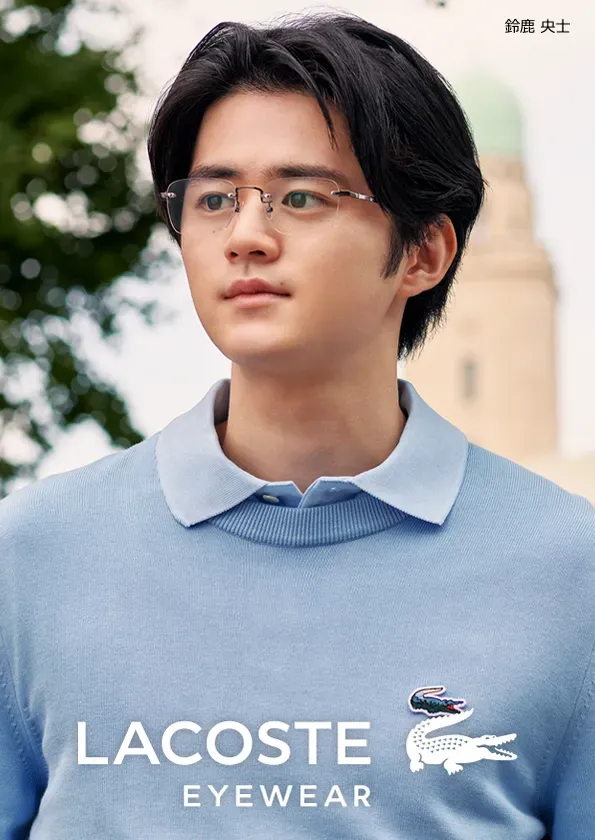 眼鏡をかけた男性が、水色のラコステのセーターを着て、カメラのほうを見ている写真