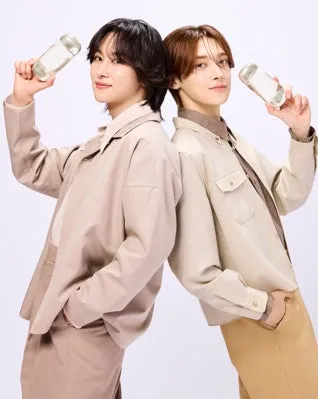 2人の男性が背中合わせで立っており、それぞれがボトルを持っています。彼らは薄い色のジャケットとパンツを着ています。