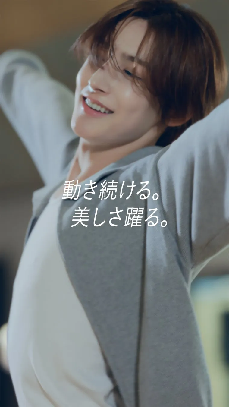 笑顔で上を見上げる男性の画像です。彼はグレーのパーカーを着ており、髪は茶色です。背景はぼやけています。