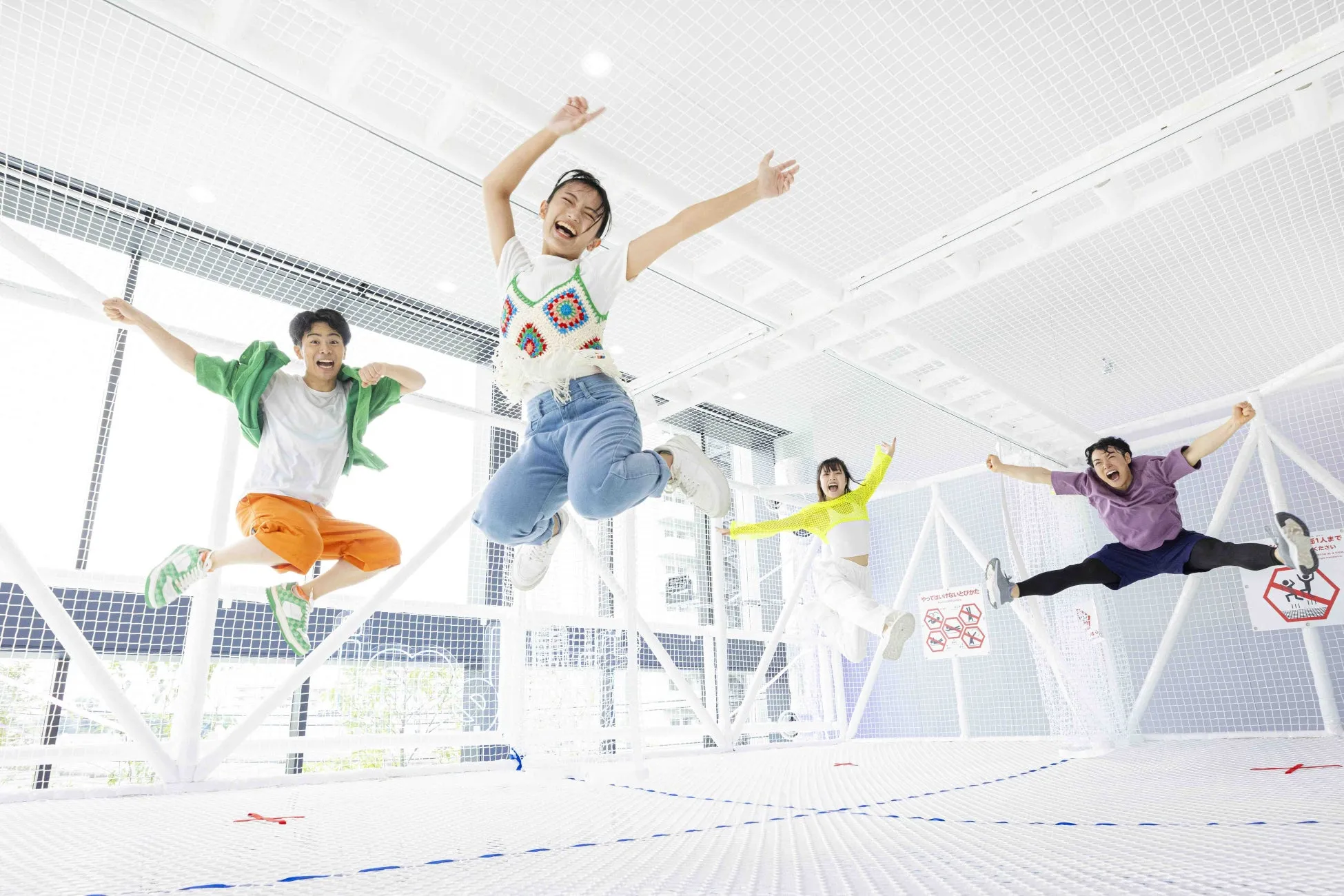 トランポリン施設でジャンプする4人の若者たち。楽しそうな表情で、空中での動きを表現している。