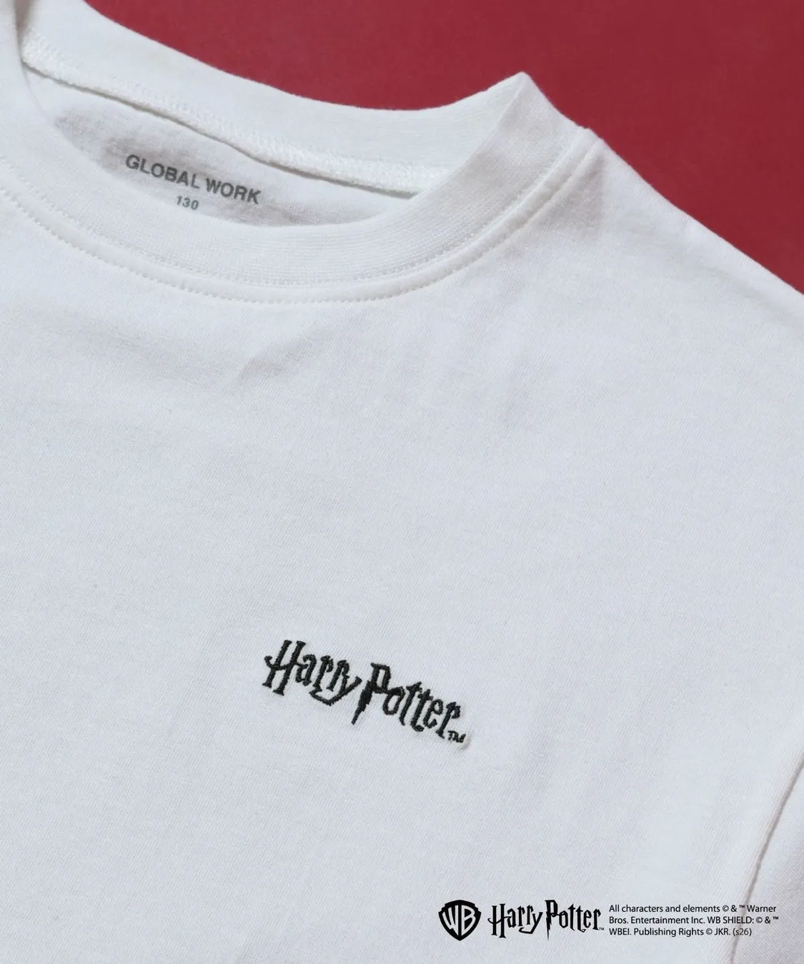 白いTシャツに「Harry Potter」のロゴが刺繍された画像。Tシャツの襟元とロゴの詳細が写っており、背景は赤色。