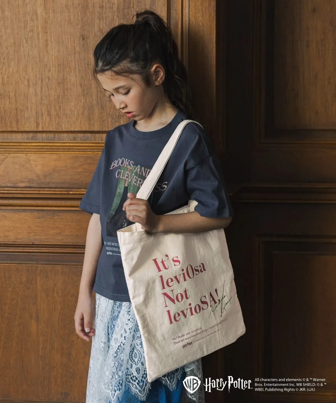 ハリーポッターのトートバッグを持った女の子の画像。彼女は紺色のTシャツと青いレースのスカートを着ています。バッグには「It's leviosa Not levioSA!」と書かれています。