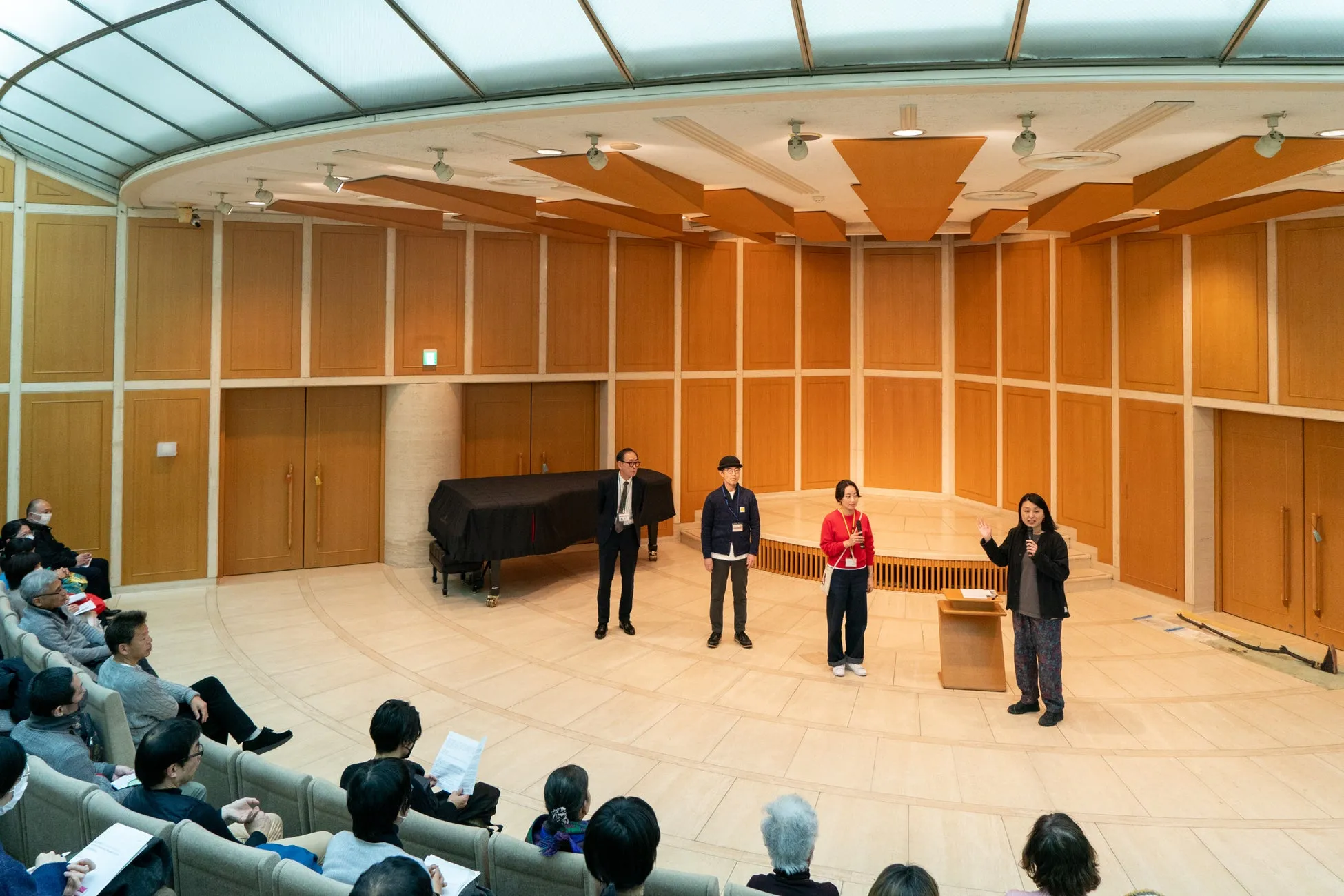 講演会または会議の様子。ステージ上に4人の人物が立っており、聴衆は客席に座っている。