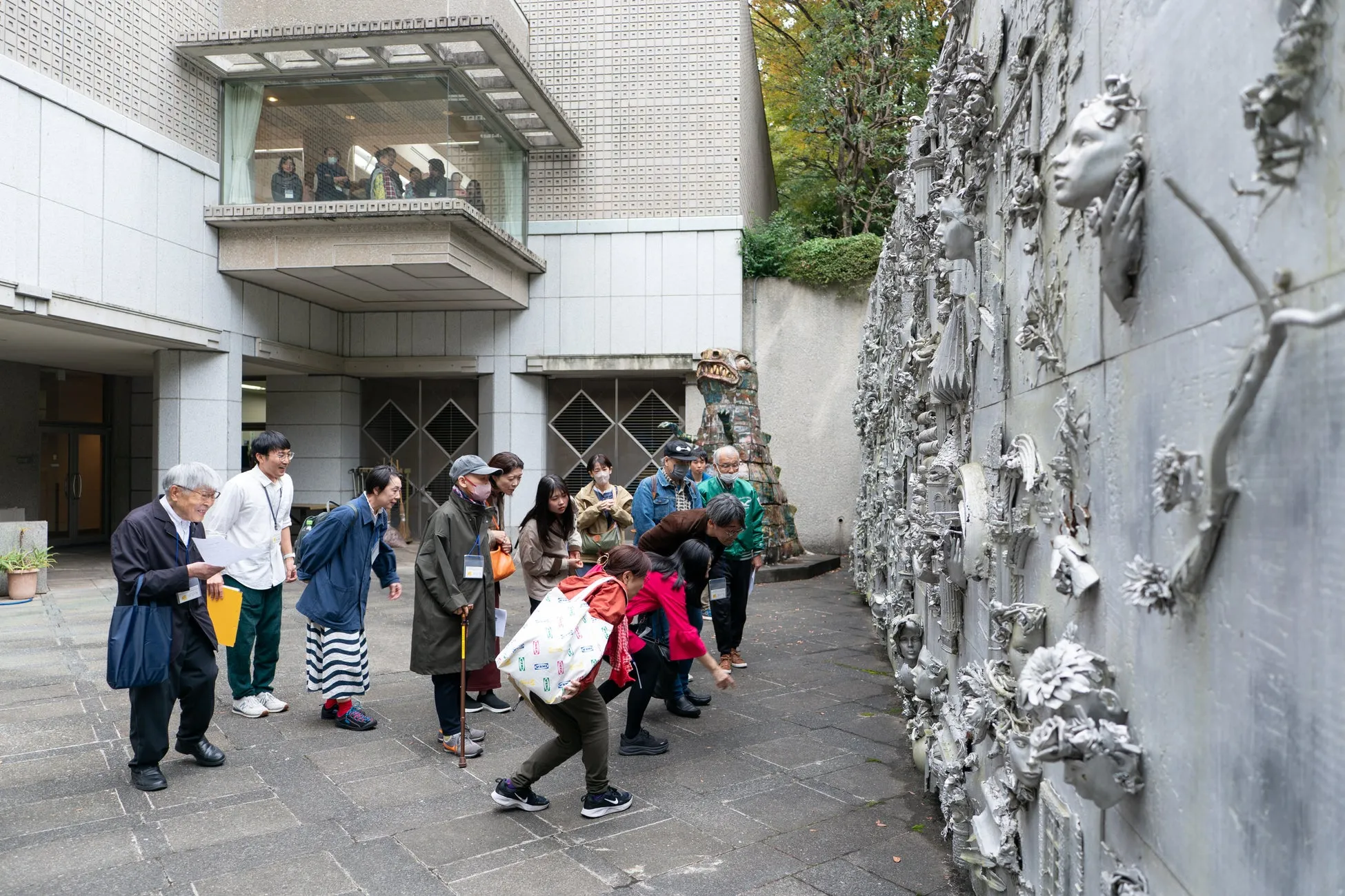 美術館を訪れた人々が、壁に展示された彫刻作品を鑑賞している様子。