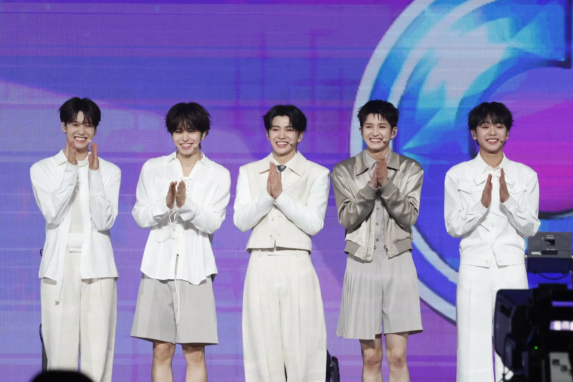5人の男性が舞台上で拍手をしており、笑顔を浮かべている。