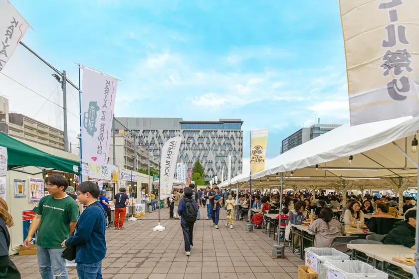 屋外のイベント会場で、多くの人々が集まって食事や飲み物を楽しんでいる様子。