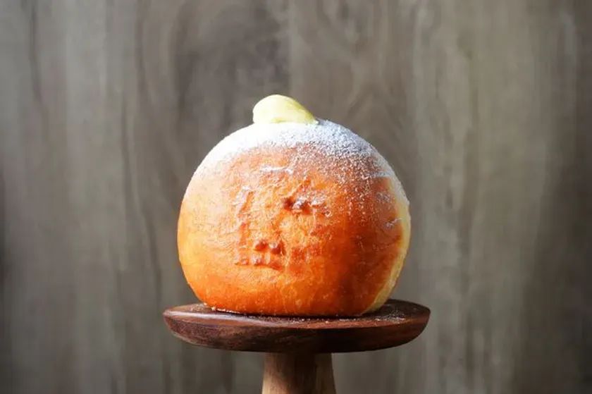 ハロウィーンをテーマにしたパン。かぼちゃの形をしており、粉砂糖がかかっている。木製の台に置かれている。