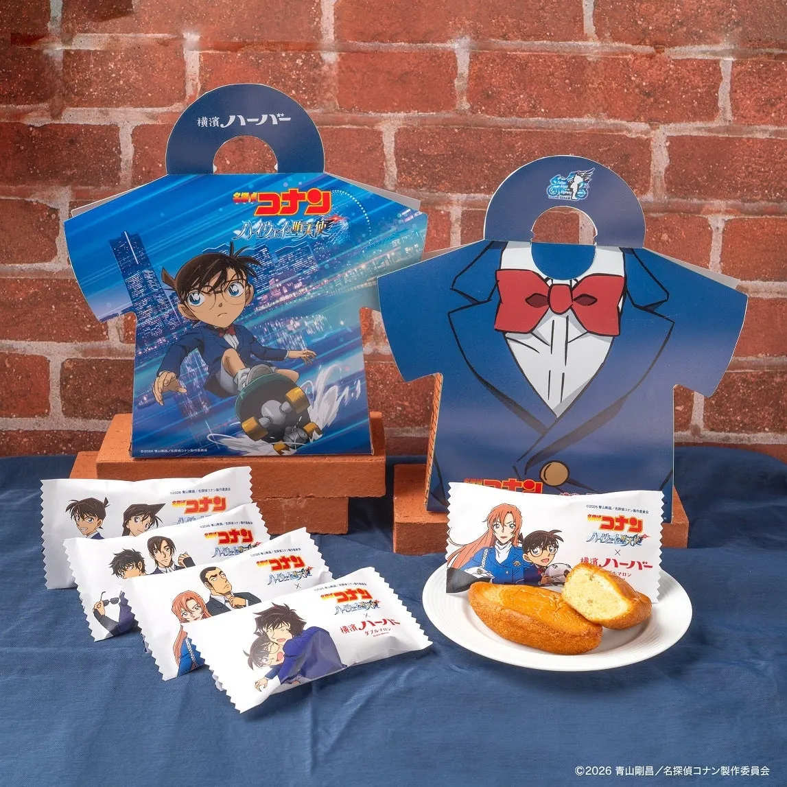 名探偵コナンのキャラクターが描かれたお菓子のパッケージと、お菓子が写った写真です。パッケージはスーツの形をしており、キャラクターが描かれています。お菓子は、ハーバーという名前で、白い袋に入っています。写真には、赤レンガの背景と、青い布が敷かれたテーブルが写っています。