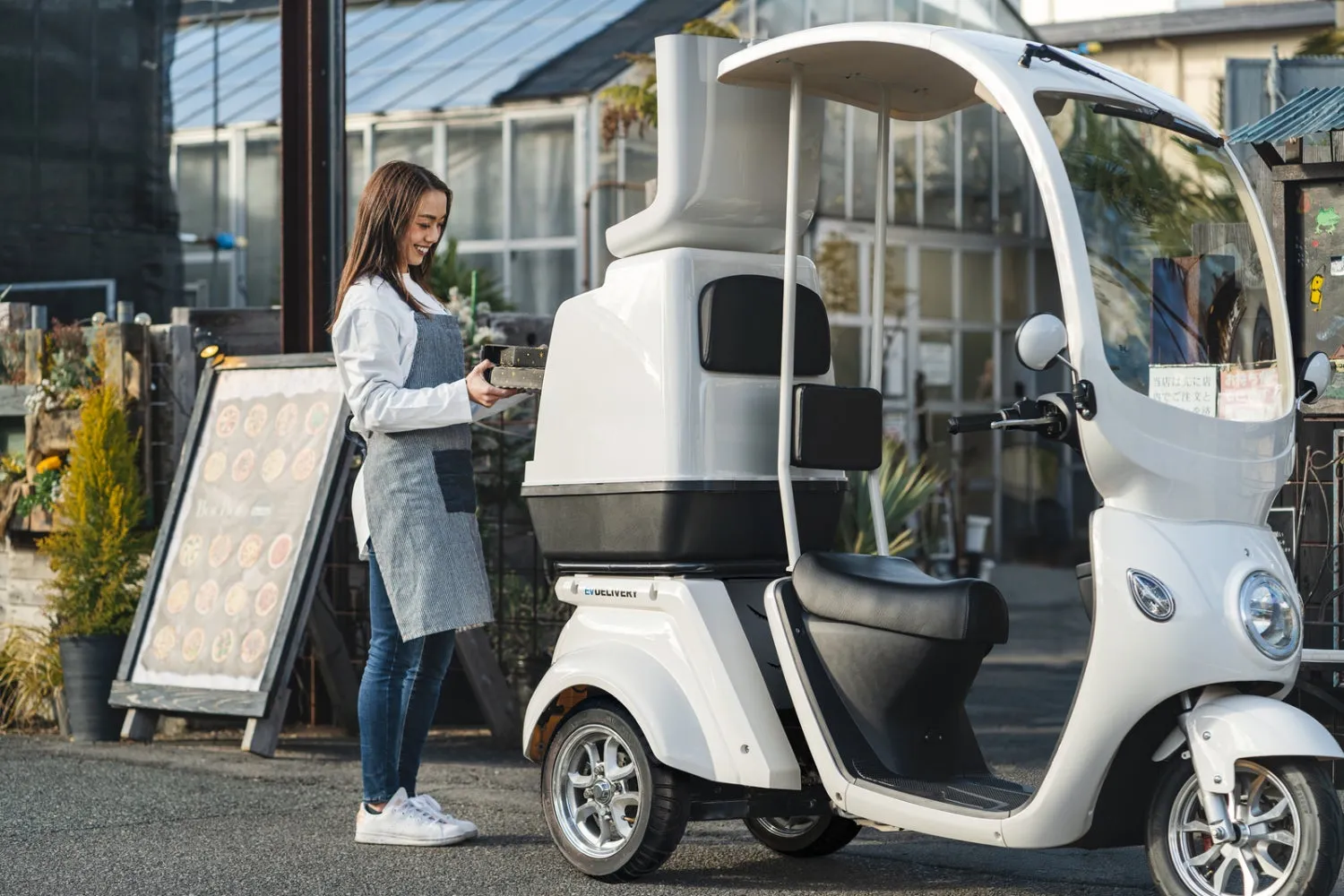 電動スクーターのそばで箱を持つ女性