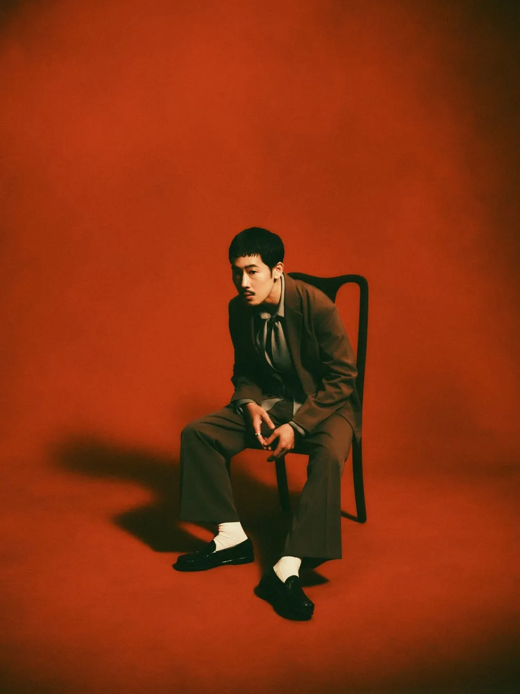 赤い背景に、スーツを着て椅子に座っている男性の写真。