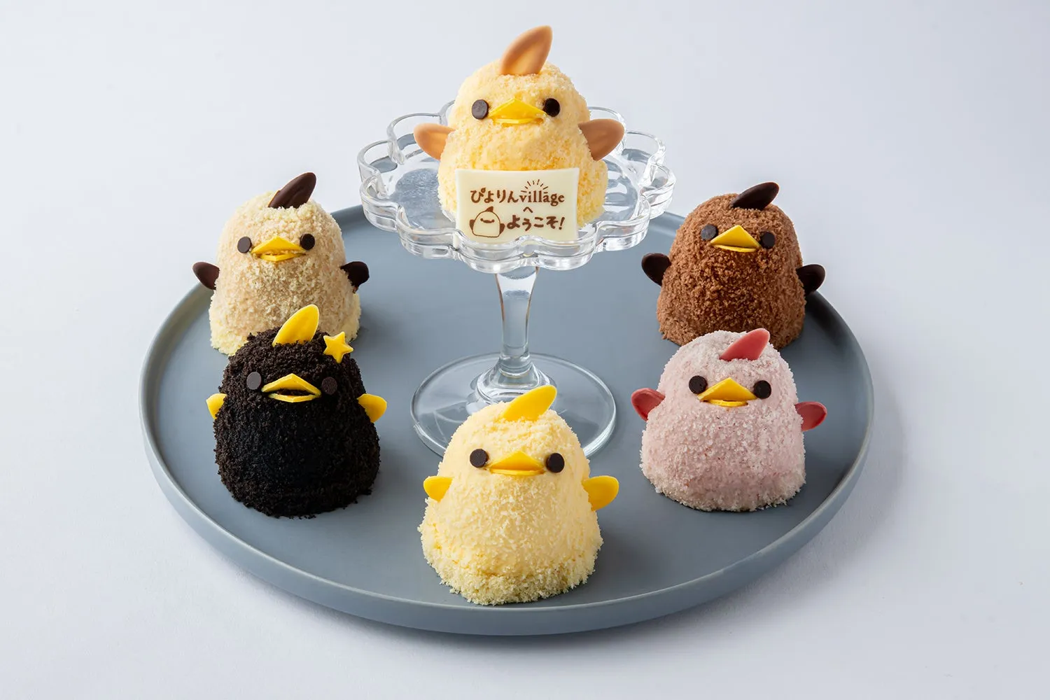 ひよこの形をした可愛らしいケーキが並んだ写真です。様々な色のケーキがあり、中央のケーキは台に乗せられています。