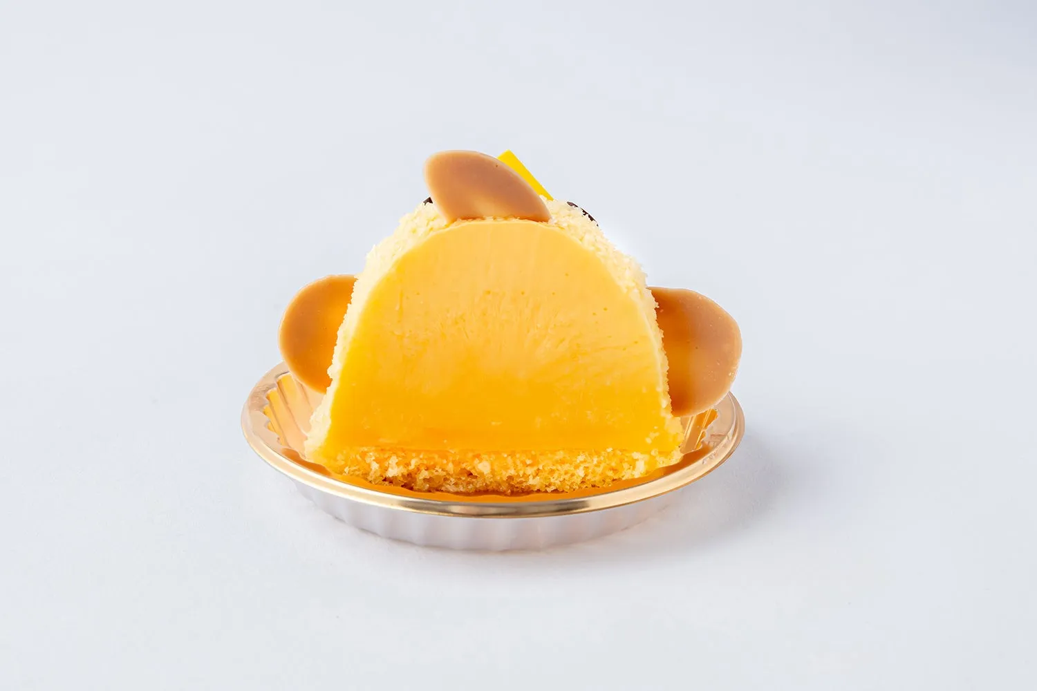 アニマルケーキのクローズアップ写真。ケーキは黄色で、耳のように見える丸いクッキーが2つ付いており、ケーキの上の装飾には黒い粒と黄色の飾りがある。