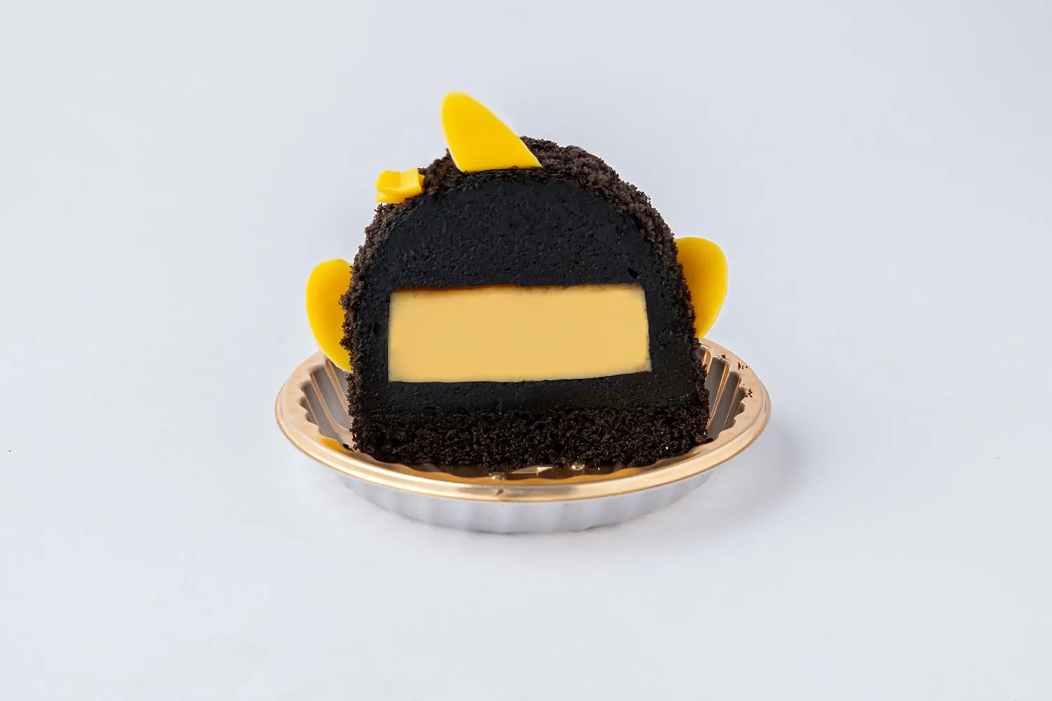ケーキの断面図。黒い生地の中に黄色いクリームが層になっており、黄色い飾りが添えられている。ケーキは金色の縁の皿に載せられている。