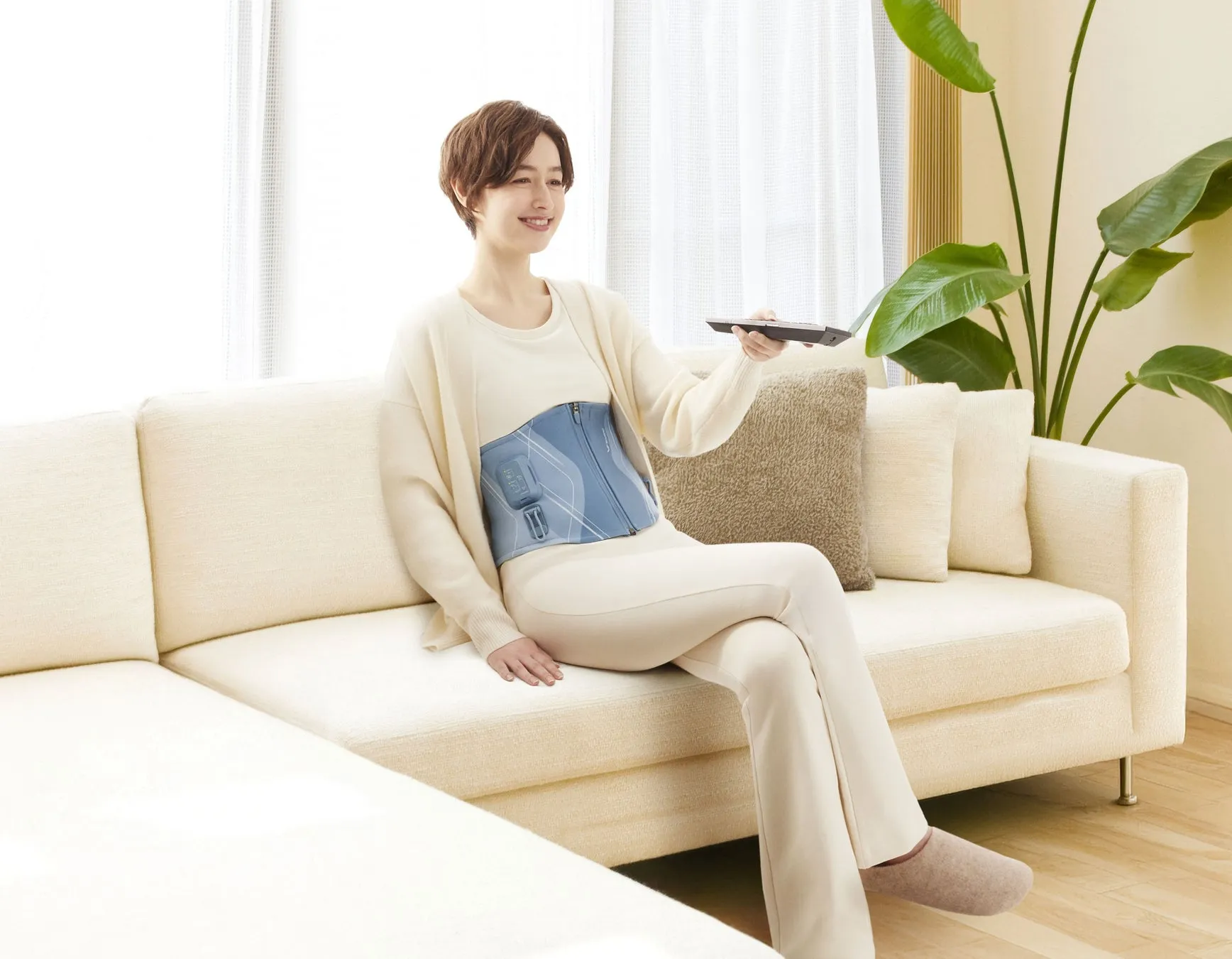 女性がソファに座り、リモコンを操作している様子。腰にはサポーターを装着