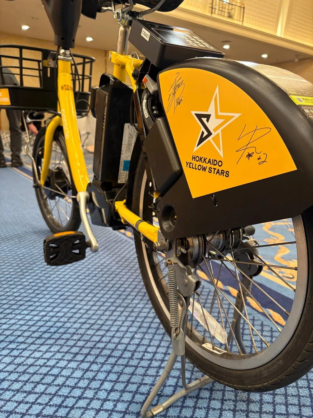 黄色い自転車。自転車のホイールの近くに「HOKKAIDO YELLOW STARS」のロゴとサインが描かれています。