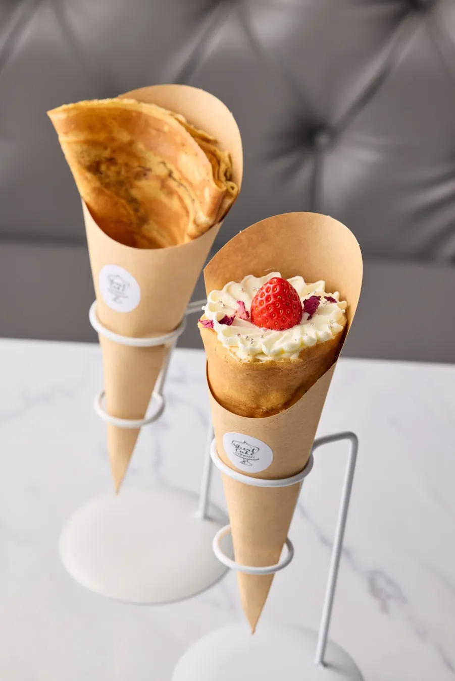 2つのコーンに入ったクレープのクローズアップ写真。一つはプレーンで、もう一つはクリームとイチゴがトッピングされています。