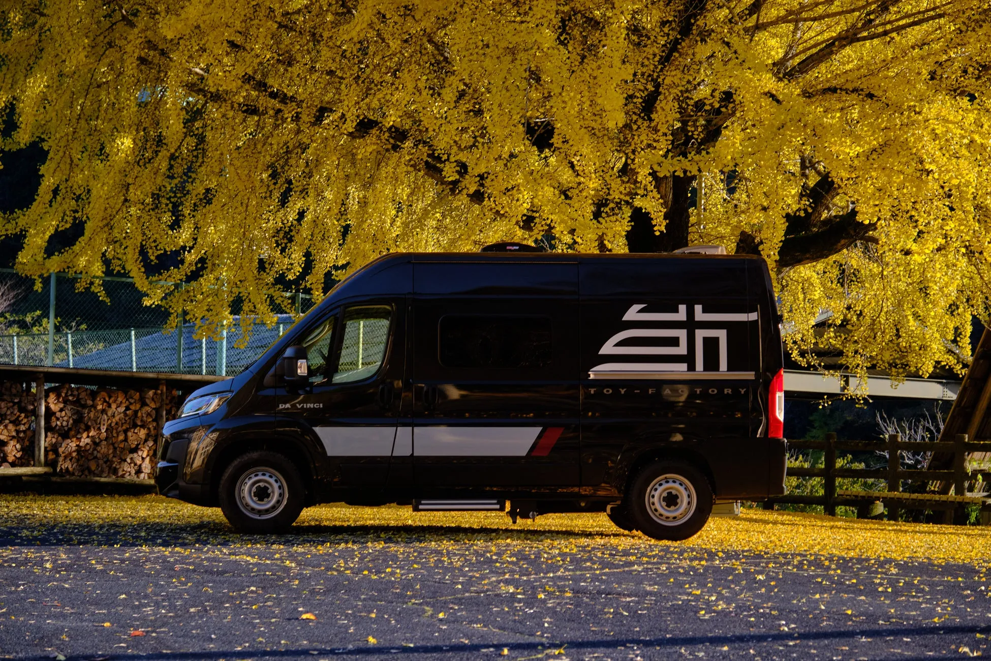 黒いキャンピングカーが黄色い葉が茂る木の下に駐車されています