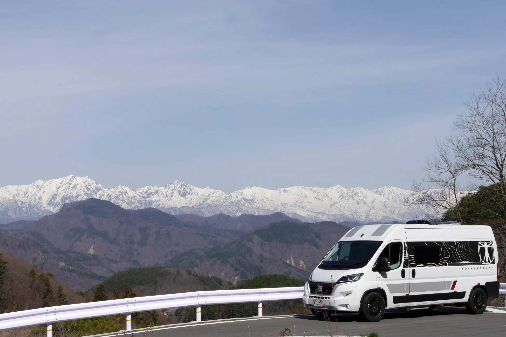 白いキャンピングカーが山道のカーブを走る写真