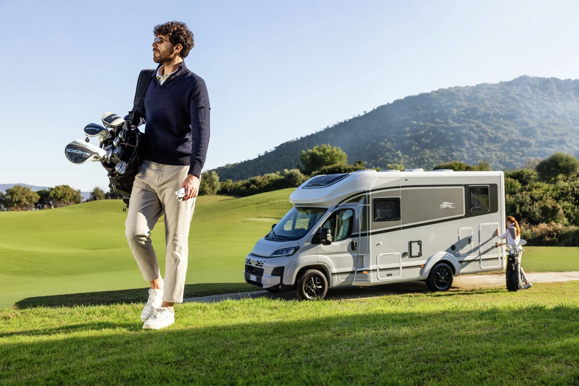 ゴルフバッグを持った男性とキャンピングカーが写った写真