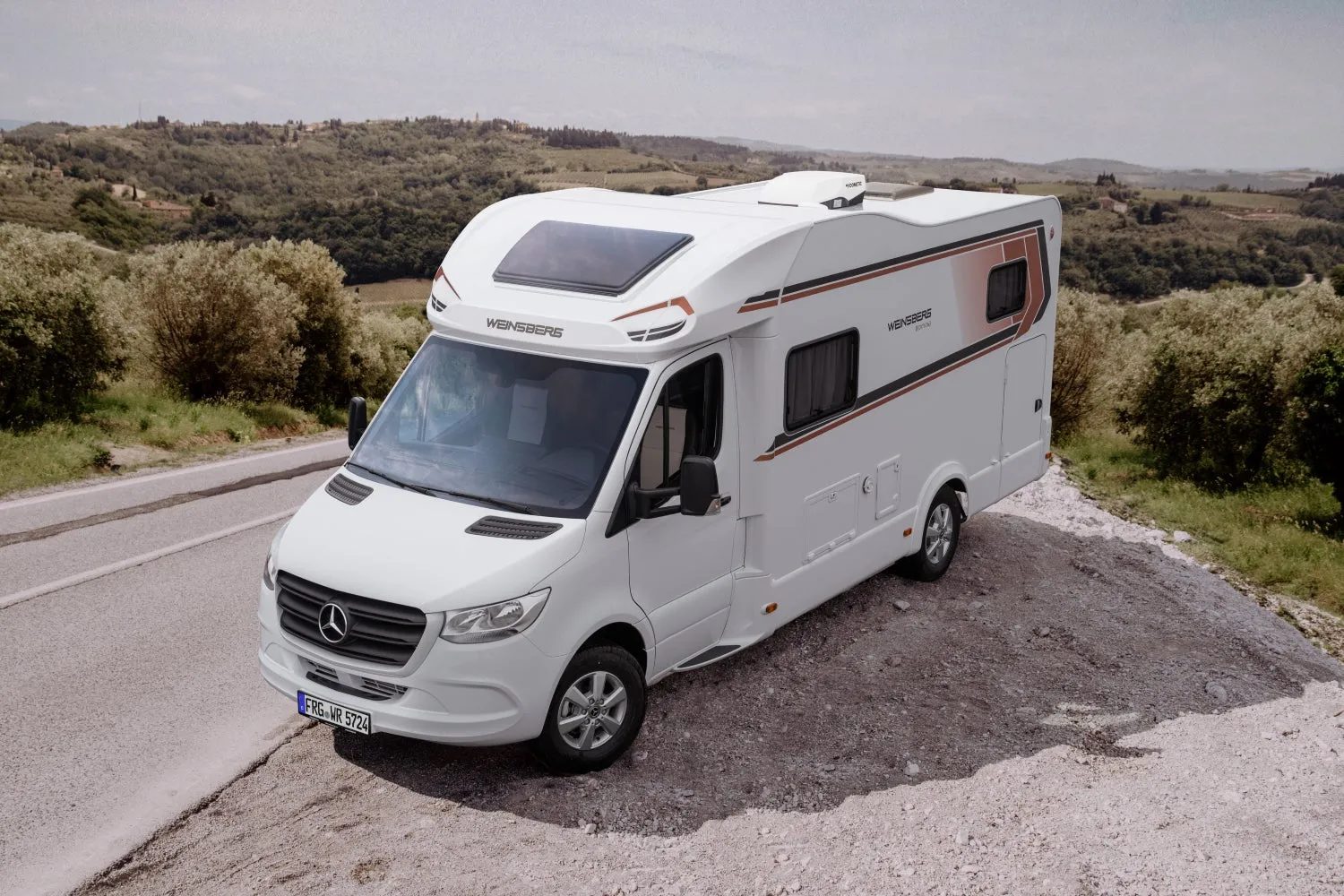 白いキャンピングカーが丘陵地帯の道路の側面に駐車している様子