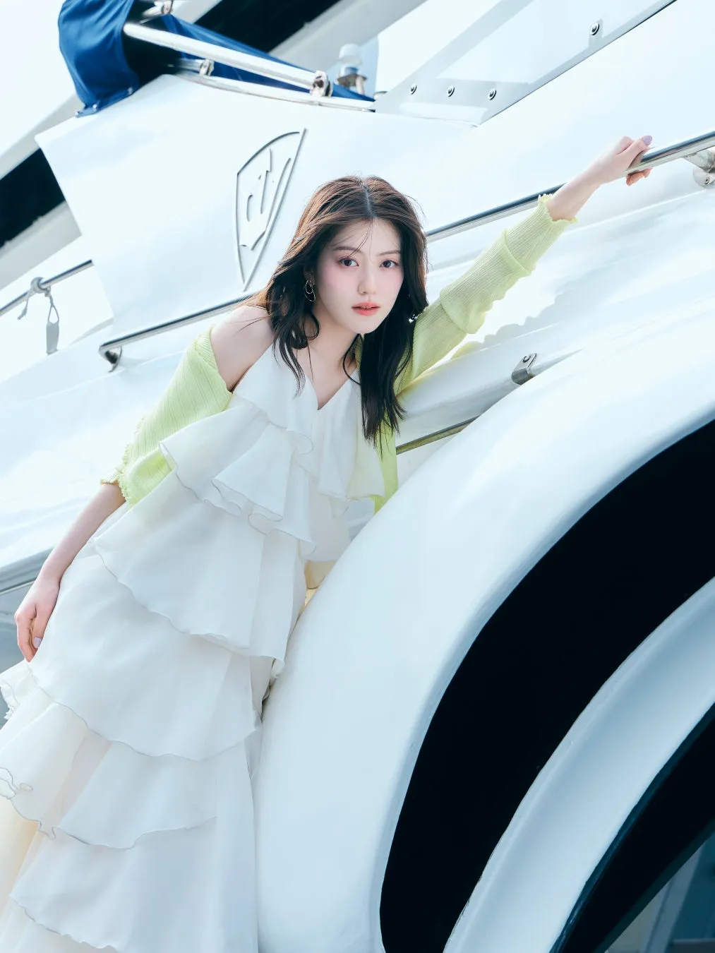 白いドレスと黄緑色のカーディガンを着て、ヨットに寄りかかる女性