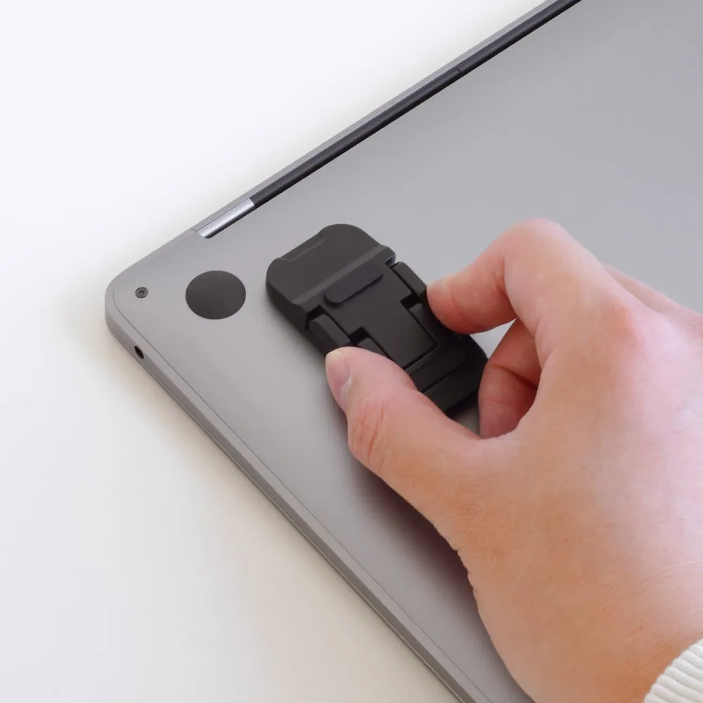 MacBookの背面に装着された、黒い折り畳み式のスタンドを手で操作している様子。
