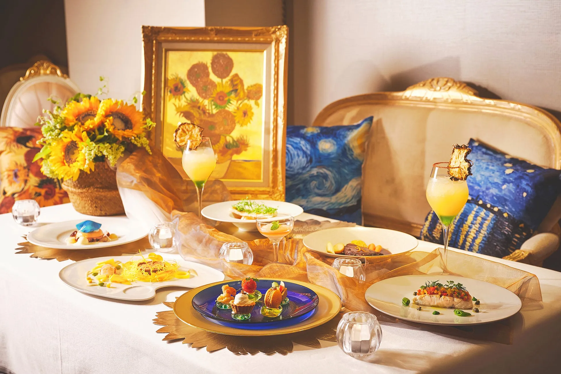 テーブルセッティングされた料理の写真。ゴージャスな雰囲気で、絵画やひまわりのアレンジメントが添えられています。料理は美しく盛り付けられており、洗練された印象を与えます。