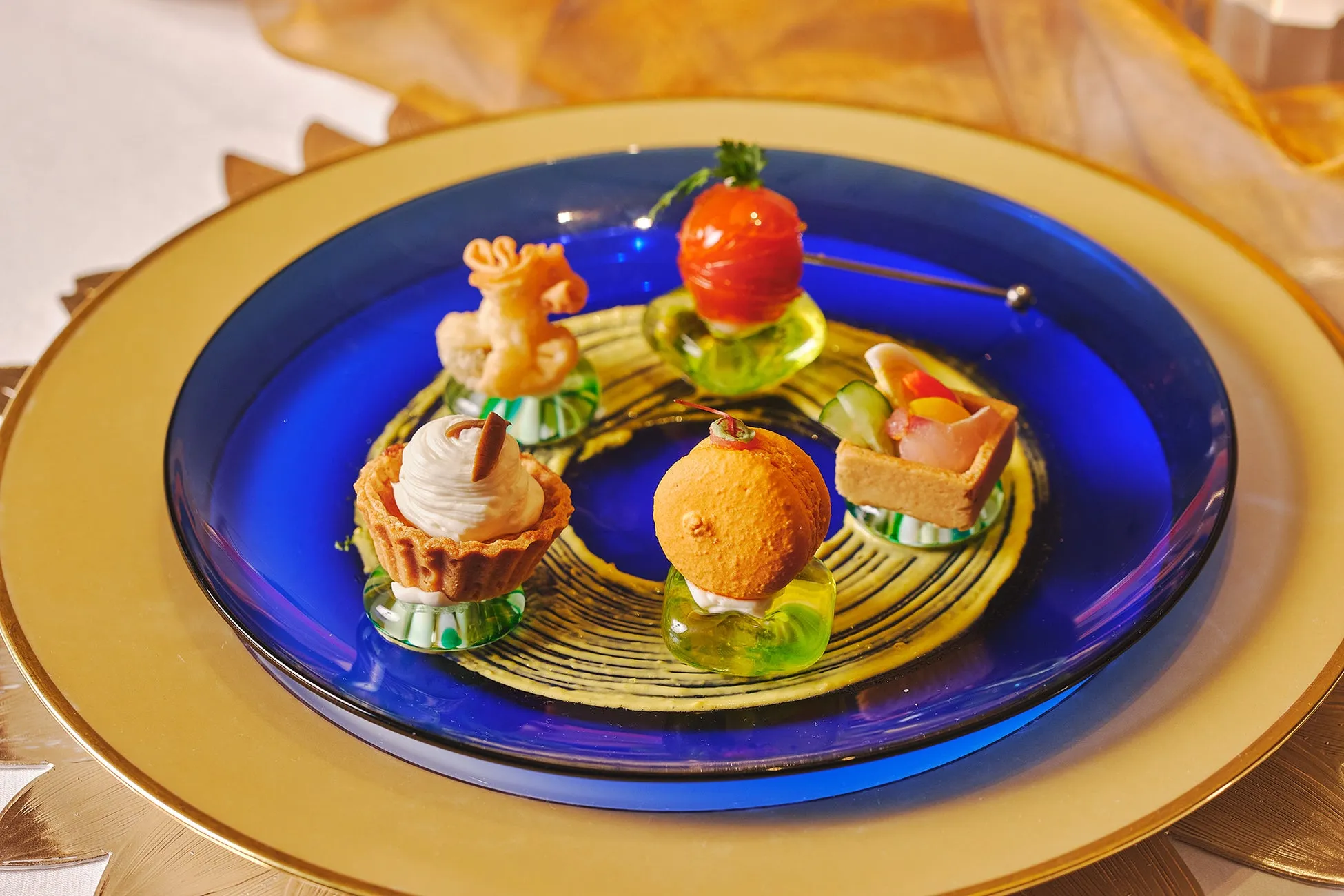 様々な食材を使った、美しく盛り付けられた一口サイズの料理が並んだ写真。青い皿に盛り付けられ、金色の縁取りが施された白い皿の上に置かれています。