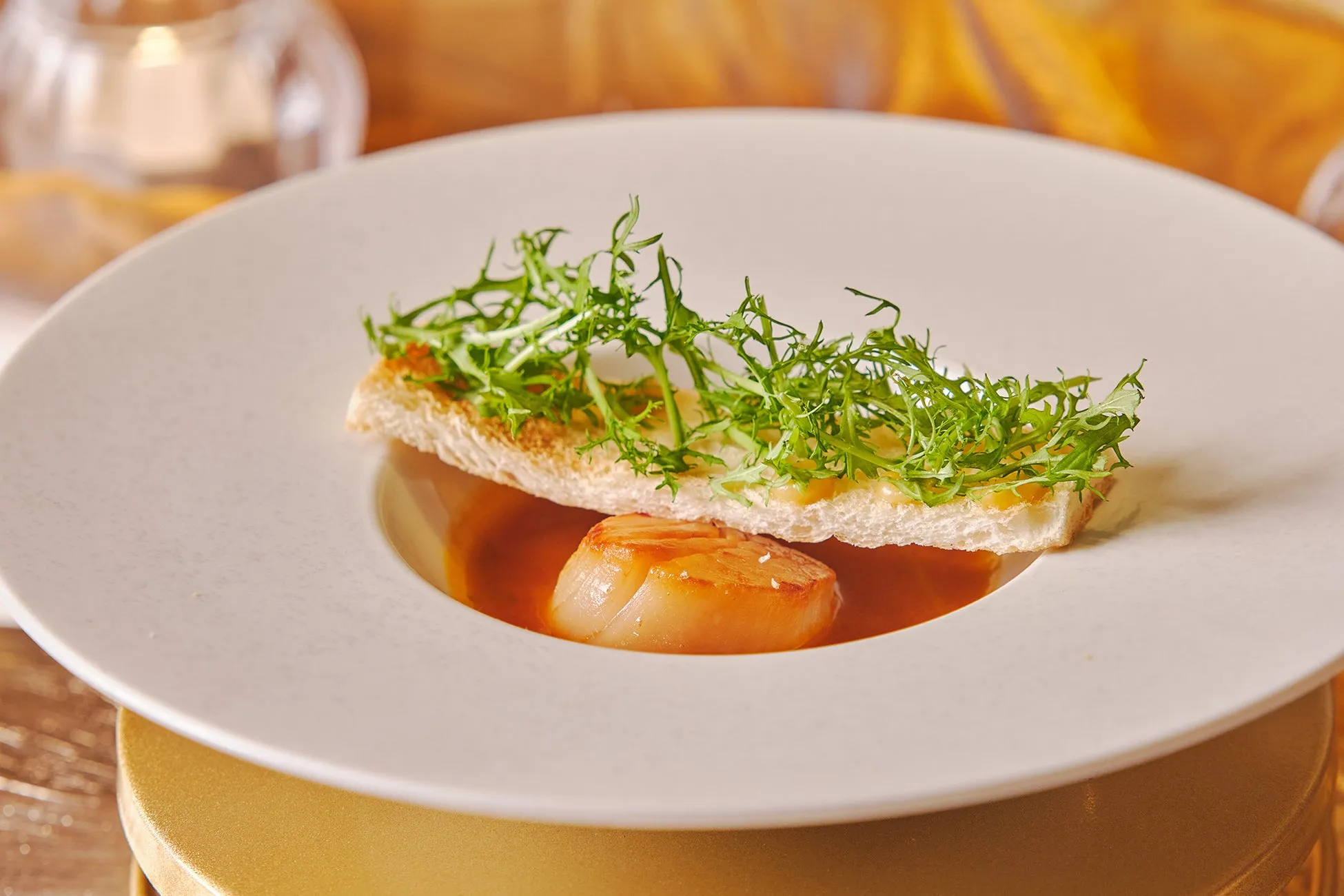 お皿に盛られた料理の写真。ホタテ、パン、葉物野菜が添えられています。