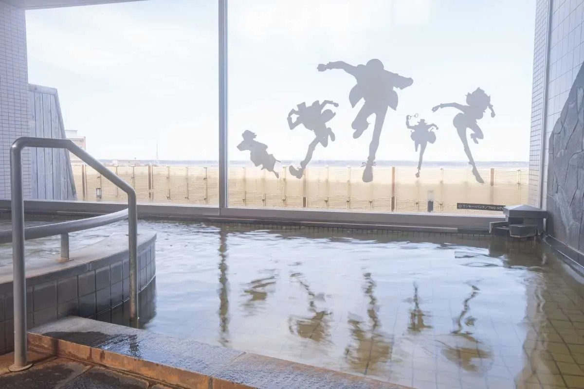 窓にシルエットが描かれた温泉施設。湯船には水面が映り込み、開放感がある