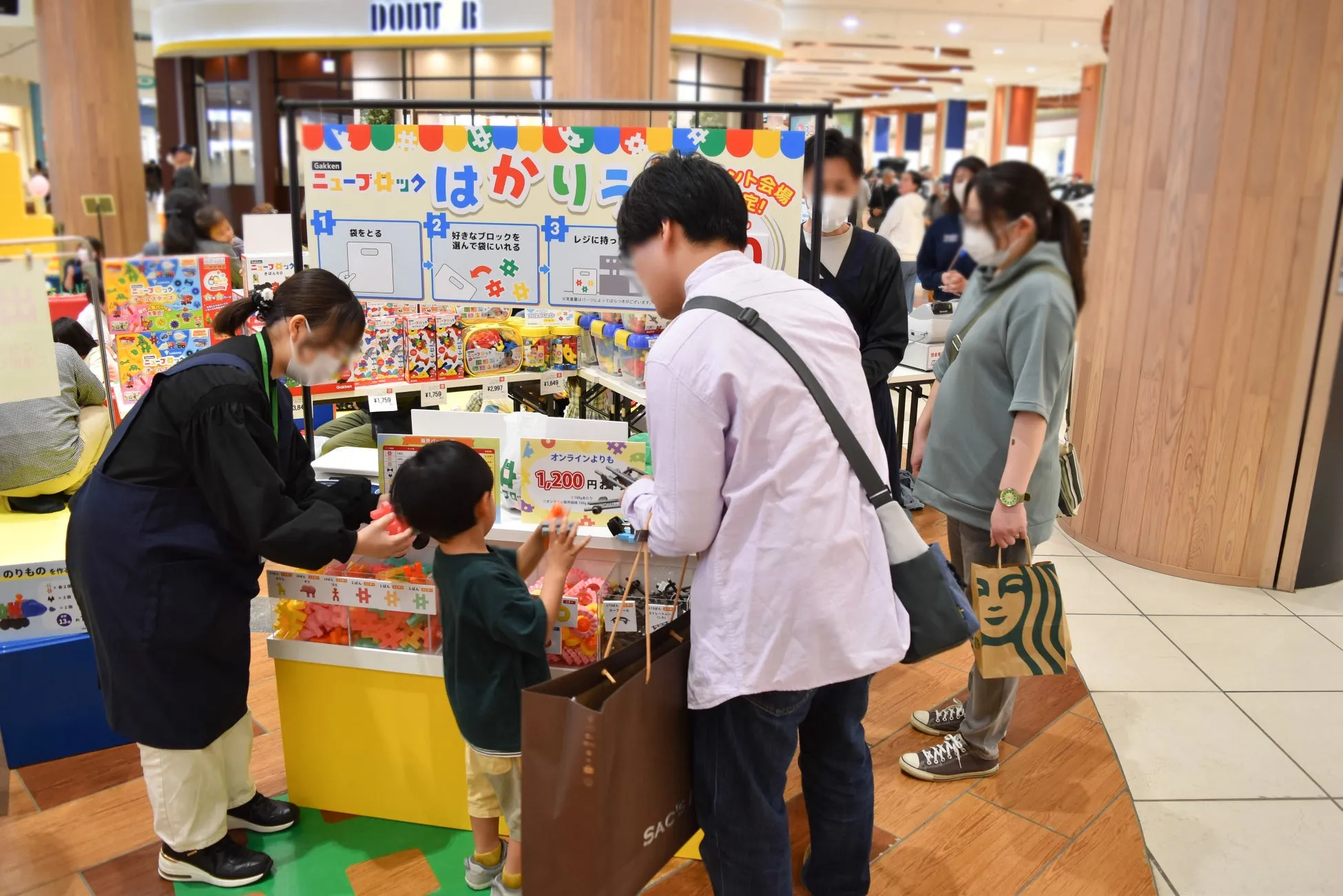 子供向けのおもちゃ売り場の様子。店員と子供、親が商品を選んでいる様子が写っています。ニューブロックのイベントのようです。