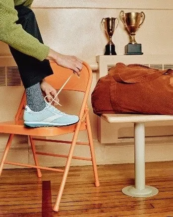 オレンジ色の椅子に座って靴紐を結ぶ人の写真。 背景にはトロフィーとバッグが見える。