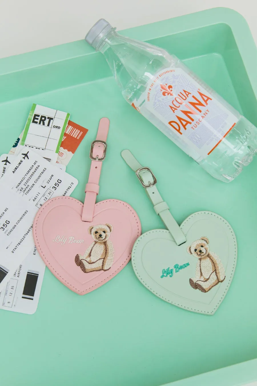 ハート型のタグ、水、チケットが写った写真。タグにはクマのイラストと「Lily Bear」の文字が描かれている。