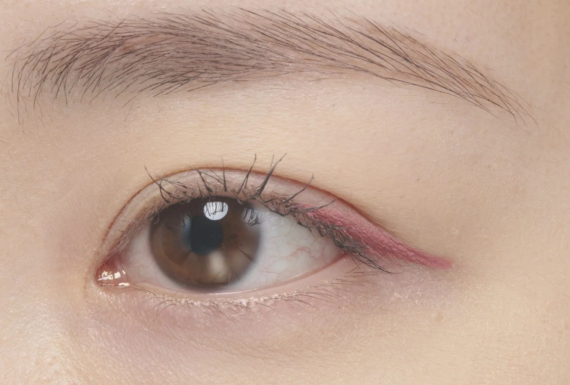 目のクローズアップ。まぶたにピンクのアイライナーが塗られ、眉毛と皮膚が写っている。