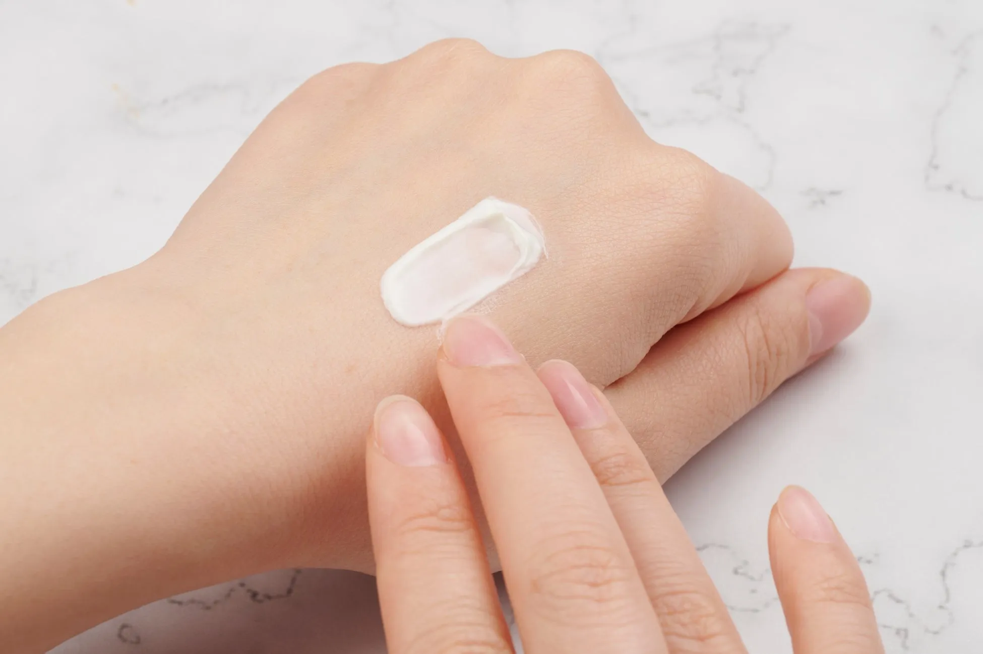 手のひらにクリームを塗っている様子を写した写真です。手は白く、背景は白大理石のようです。