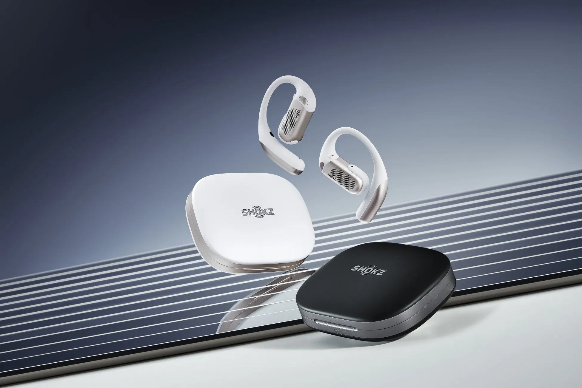 白と黒のShokzワイヤレスイヤホンと充電ケースが、斜めの線が描かれた背景に配置された写真です。