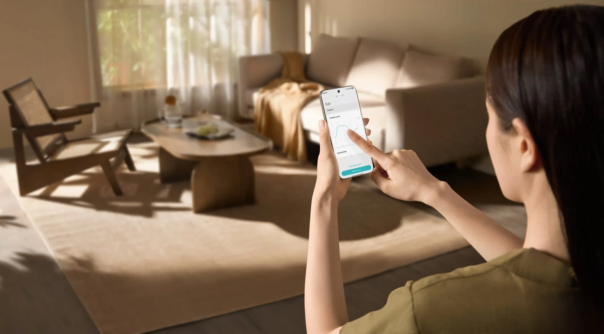 女性がスマートフォンでグラフを操作している様子。背景にはリビングルームがあり、ソファやテーブル、椅子などが配置されている。