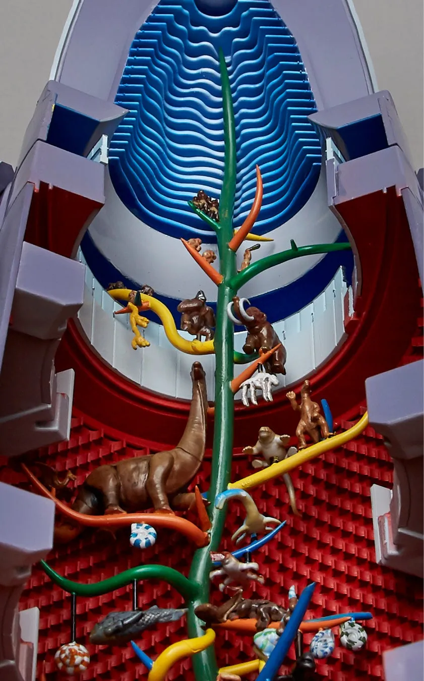 カラフルな装飾の中に、恐竜や動物のフィギュアが配置された芸術的な作品です。中央には緑色の幹があり、そこから様々な色の枝が伸びています。枝にはさまざまな動物のフィギュアが配置され、その周りを装飾が囲んでいます。