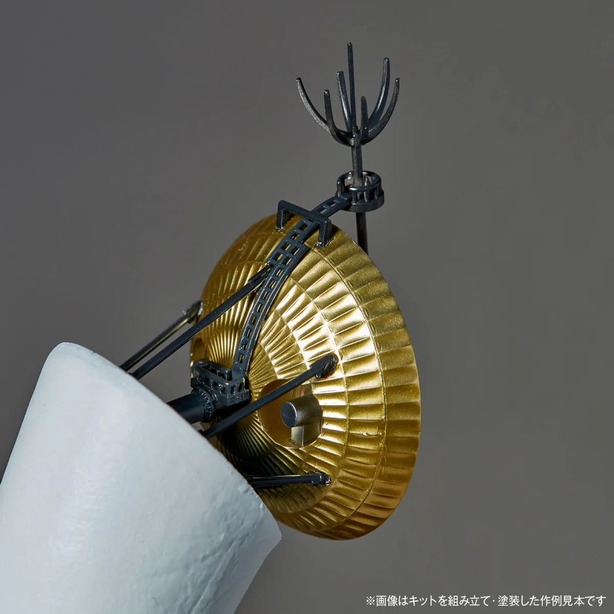 金色のアンテナと白い円錐形の物体が写った写真。背景はグレー。