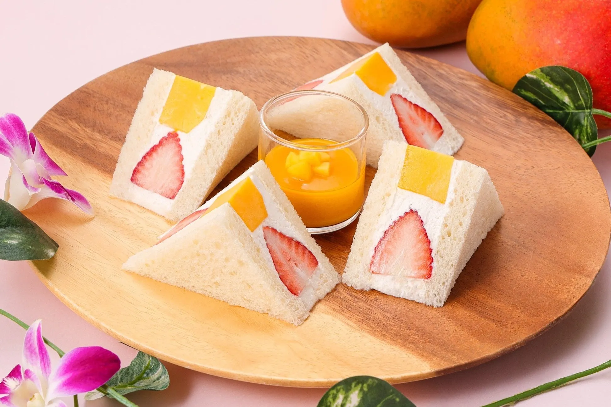 木製の皿に、イチゴとマンゴーを挟んだサンドイッチとマンゴーソースが乗っている写真です。