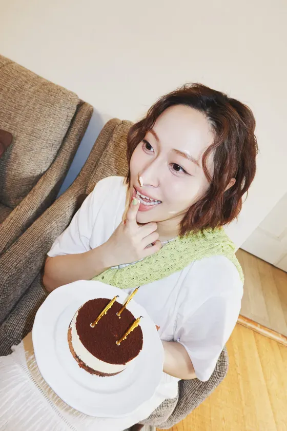 ケーキを持った女性の写真。女性は指を口に当てており、顔にはクリームが付いている。誕生日のように見える。