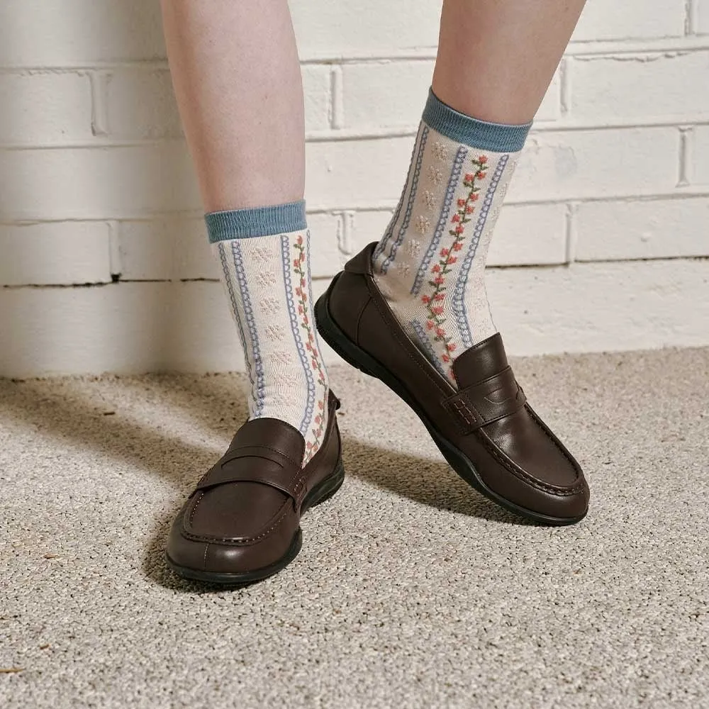 茶色のローファーを履いた足と、花柄の靴下のクローズアップ写真。背景には白いレンガの壁がある。