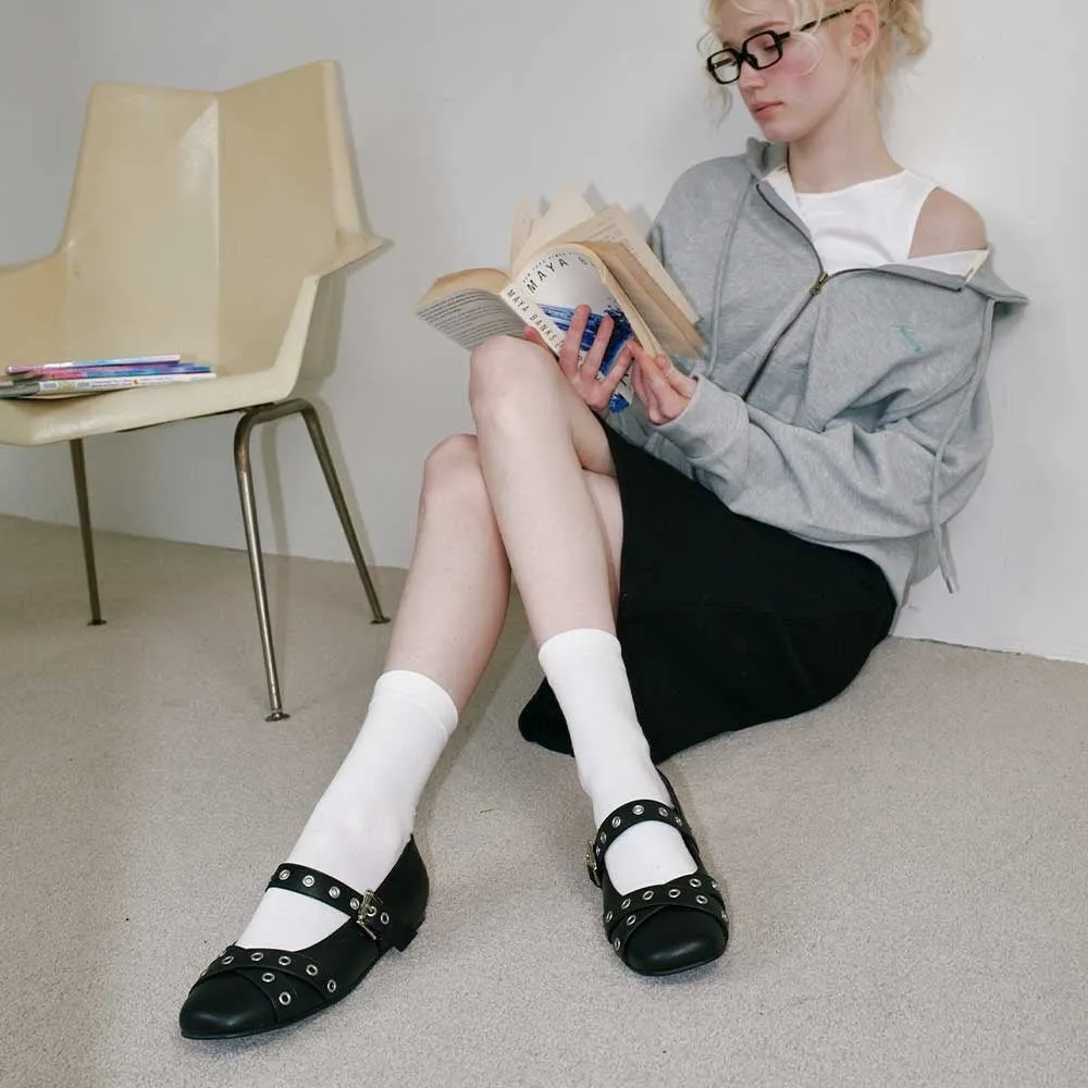 読書する女性の写真。彼女は黒いスカート、白い靴下、黒い靴を履いており、眼鏡をかけています。彼女は本のページをめくっており、読書に集中しています。彼女の周りには、椅子と本があります。