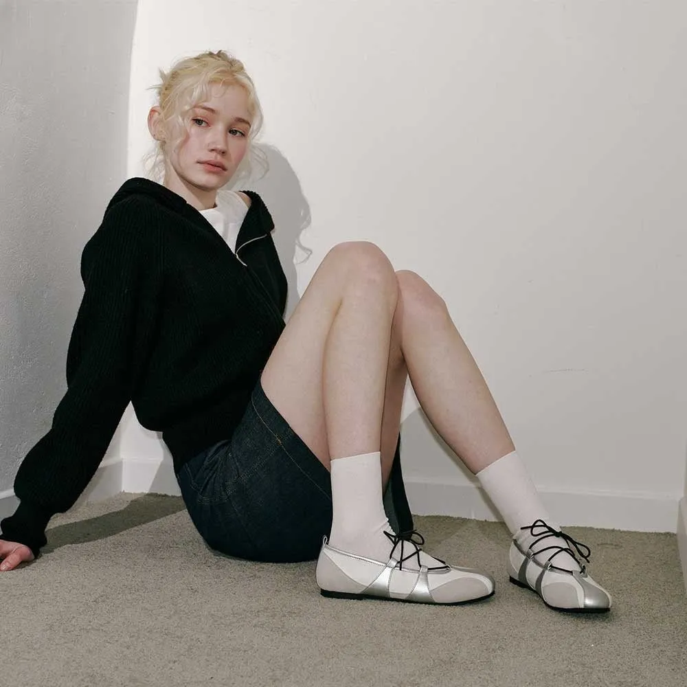 床に座っている女性の写真。彼女は黒いフード付きジャケット、デニムのスカート、白い靴下、白い靴を履いています。彼女は金髪で、カメラを見ています。