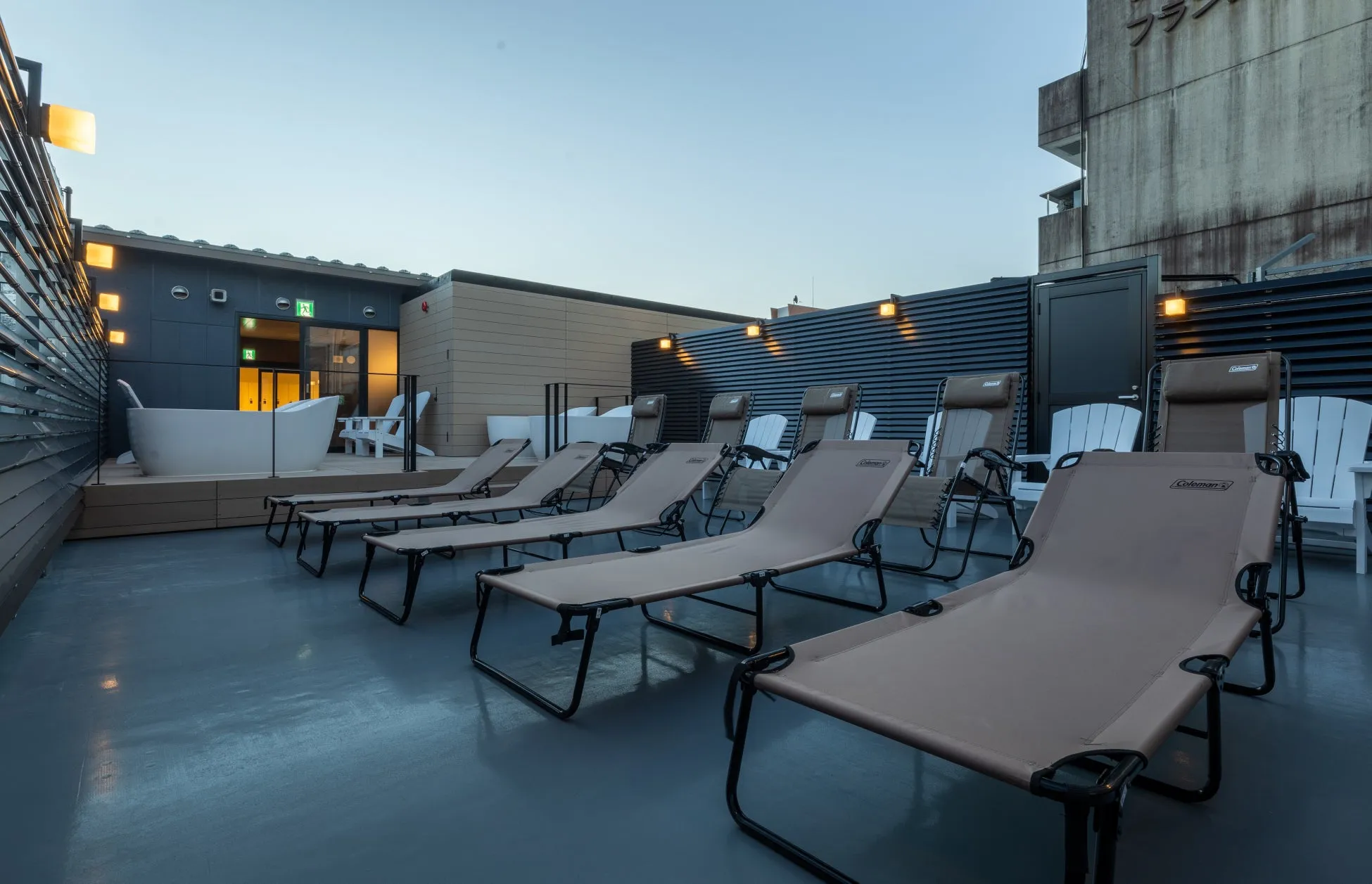 屋上のリゾート空間の写真。多くのリクライニングチェアが並び、奥にはジャグジーと白い椅子が配置されている。夕暮れ時の空が背景に広がり、リラックスした雰囲気を醸し出している。