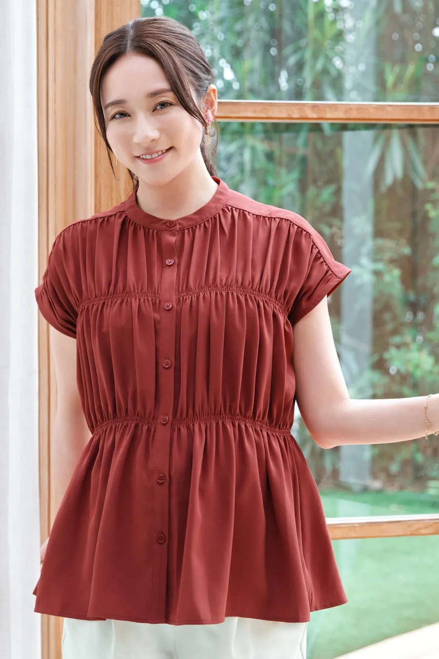 窓際に立つ女性。赤いブラウスを着て微笑んでいる。