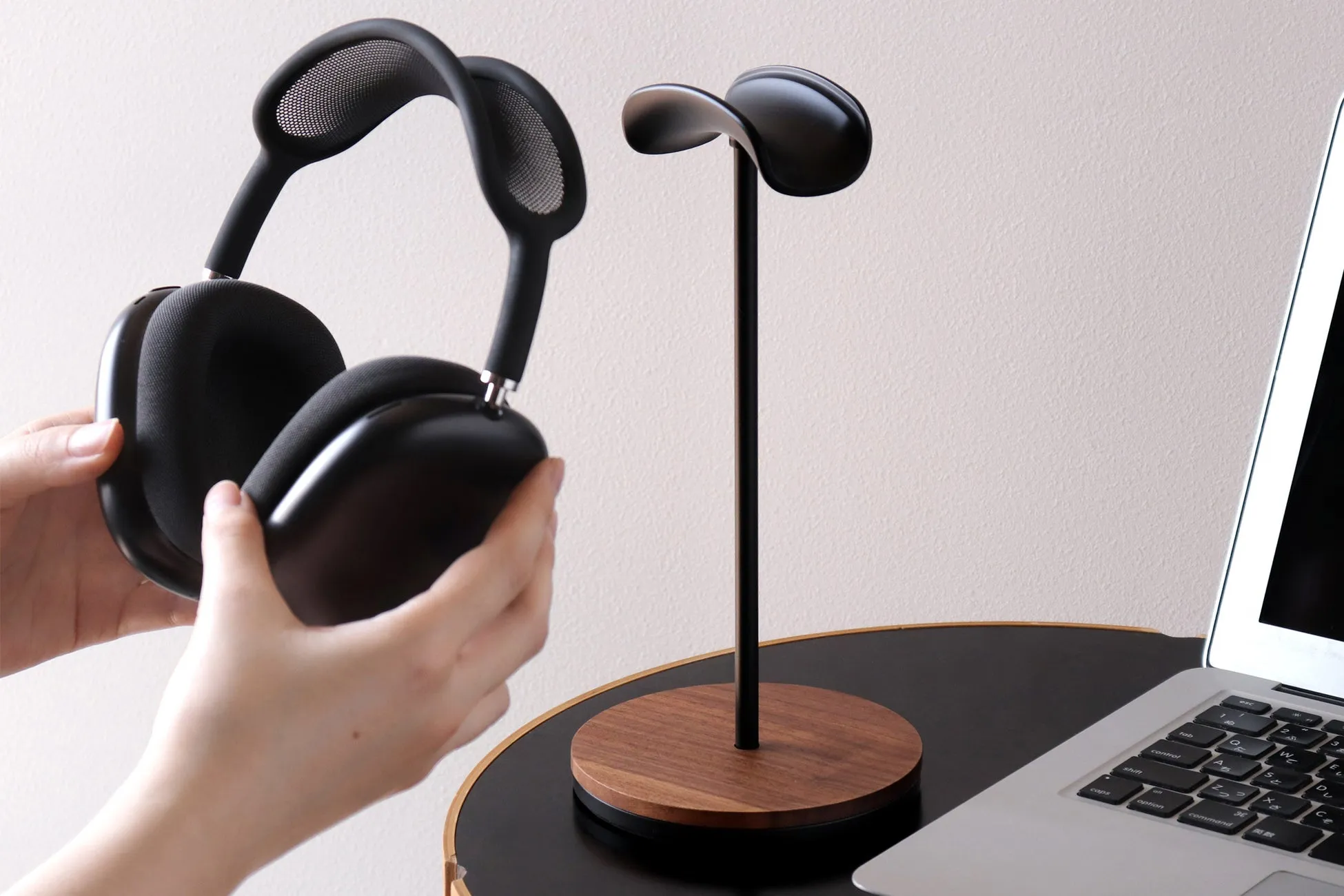 黒いヘッドホンとヘッドホンスタンドの写真。ヘッドホンは人の手で持たれており、スタンドに置かれる様子が写っています。