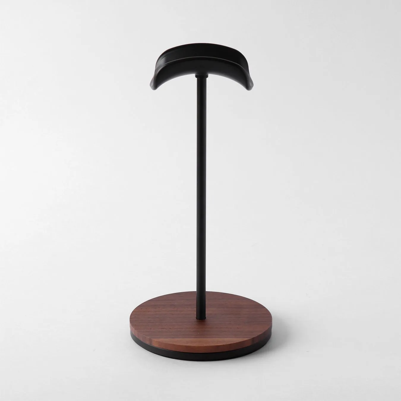 ヘッドホンスタンドの画像。黒いT字型のスタンドで、上部はヘッドホンのヘッドバンドを支えるようにカーブしており、下部は丸い木製のベースに固定されている。